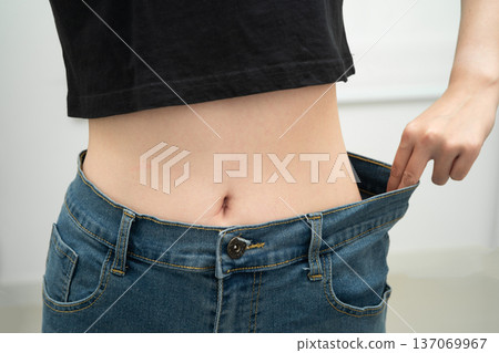 Young Asian woman losing weight wearing loose pants in oversize jeans. Young Asian woman losing weight wearing loose pants in oversize jeans. 137069967