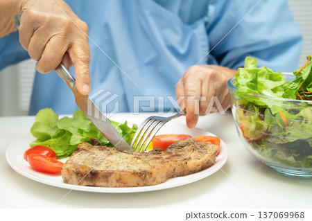 Asian elderly woman patient eating pork chop stake and vegetable salad for healthy food in hospital. Asian elderly woman patient eating pork chop stake and vegetable salad for healthy food in hospital. 137069968