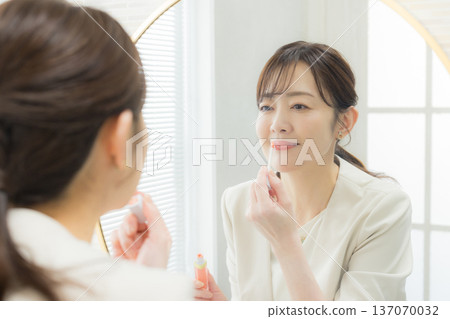 Woman applying makeup in the mirror 137070032