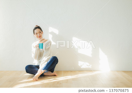 Young woman sitting on the floor and drinking coffee Young woman sitting on the floor and drinking coffee 137070875