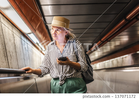Middle-aged woman checking smartphone while riding escalator in subway passage 137071172