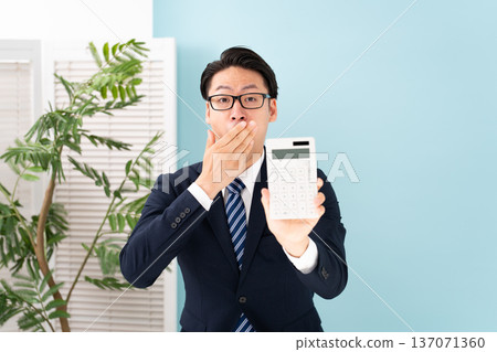 Surprised man holding a calculator 137071360