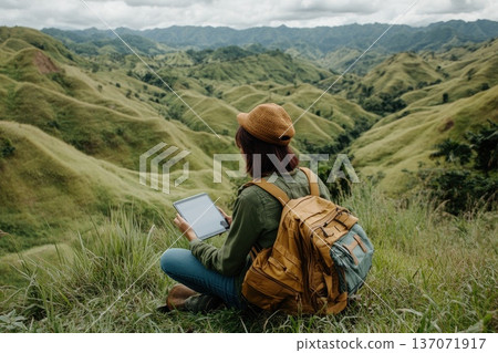 Entrepreneur Sitting on Mountaintop with Digital Device Amidst Scenic Landscape Entrepreneur Sitting on Mountaintop with Digital Device Amidst Scenic Landscape 137071917