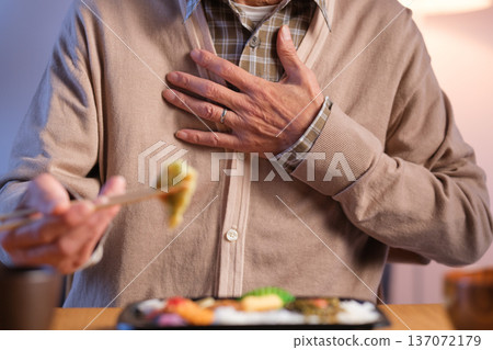 一位老年男子正在吃午飯，突然胃部不適，伸手去拿東西 137072179