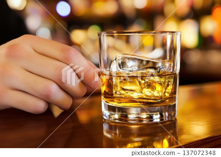 Elegant Close-Up of Hand Holding a Glass with Ice in a Stylish Bar Setting 137072348