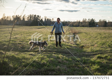Woman walking dog on leash during countryside hike in green spring meadow 137072731