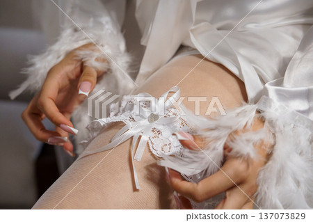 Elegant White Wedding Garter with Lace and Feather Details on Bride's Leg in Soft Lighting Elegant White Wedding Garter with Lace and Feather Details on Bride's Leg in Soft Lighting 137073829