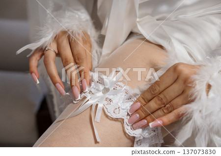 Elegant Bride Wearing White Lace Garter and Feathered Robe with Pink Nail Art in Soft Natural Light Elegant Bride Wearing White Lace Garter and Feathered Robe with Pink Nail Art in Soft Natural Light 137073830