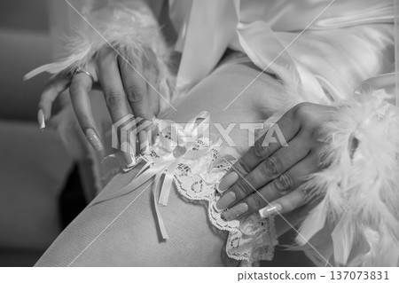 Elegant Black and White Portrait of a Bride's Hands Adorning a Lace Garter with Feathers and Ring Elegant Black and White Portrait of a Bride's Hands Adorning a Lace Garter with Feathers and Ring 137073831