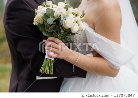 Elegant Bride Holding White Rose Bouquet with Eucalyptus in Outdoor Wedding Scene Elegant Bride Holding White Rose Bouquet with Eucalyptus in Outdoor Wedding Scene 137073847