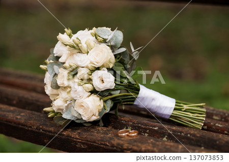 Elegant White Wedding Bouquet with Eucalyptus and Roses on Rustic Wooden Bench in Natural Setting 137073853