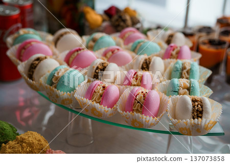 Colorful Macarons in Paper Cups Displayed on Glass Tray at Elegant Dessert Buffet with Pastel Hues and Textured Fillings Colorful Macarons in Paper Cups Displayed on Glass Tray at Elegant Dessert Buffet with Pastel Hues and Textured Fillings 137073858