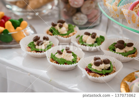 Colorful Mini Dessert Tarts with Green Icing and Chocolate Candies on White Table for Party or Celebration Colorful Mini Dessert Tarts with Green Icing and Chocolate Candies on White Table for Party or Celebration 137073862