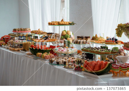 Elegant Buffet Table Overflowing with Assorted Desserts, Fruits, and Pastries in a Bright White-Room Setting 137073865