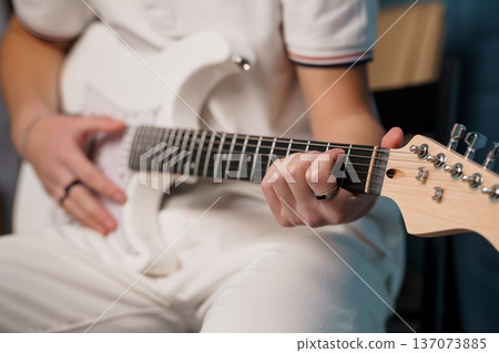 Close-up of a young man playing white electric guitar, focused hand movements, modern music performance, clean aesthetic, soft lighting 137073885