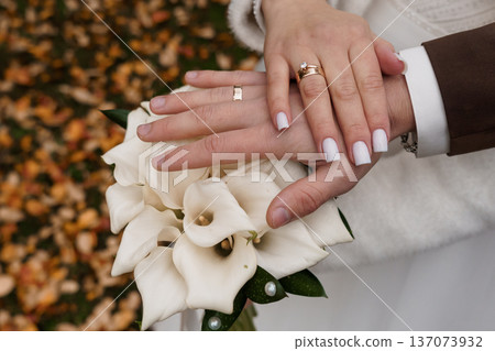 Close-up of Wedding Couple's Hands Holding White Calla Lilies Amid Autumn Leaves, Symbolizing Love and Marriage 137073932
