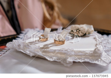 Elegant Gold Wedding Rings on White Lace Pillow with Rose Bouquet and Soft Pink Background 137073945