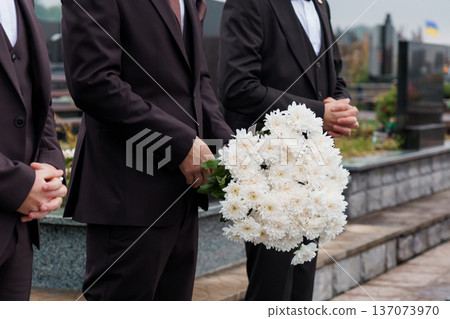 Men in Black Suits Holding White Chrysanthemums at a Cemetery During a Memorial Service 137073970