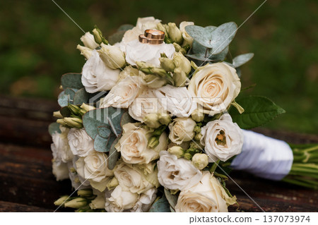 Elegant White Rose Wedding Bouquet with Gold Rings and Eucalyptus Leaves on Wooden Bench Elegant White Rose Wedding Bouquet with Gold Rings and Eucalyptus Leaves on Wooden Bench 137073974