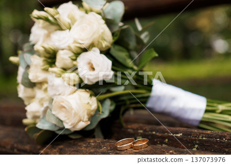 White Rose Wedding Bouquet with Gold Rings on Wooden Surface in Natural Outdoor Setting 137073976