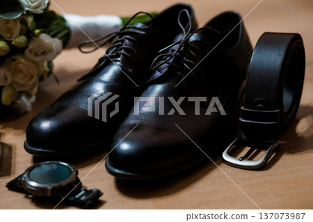 Black Dress Shoes and Belt with Watch and Bouquet on Wooden Surface Wedding Preparation Scene 137073987