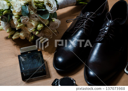 Elegant wedding groom's accessories with black dress shoes, perfume bottle, watch, and white floral bouquet on wooden surface Elegant wedding groom's accessories with black dress shoes, perfume bottle, watch, and white floral bouquet on wooden surface 137073988