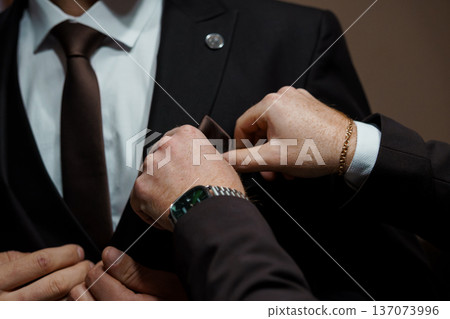 Close-Up of a Man Adjusting His Brown Tie and Pocket Square in a Black Suit with White Shirt Close-Up of a Man Adjusting His Brown Tie and Pocket Square in a Black Suit with White Shirt 137073996