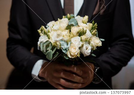 Elegant White Rose Bouquet Held by Groom in Black Suit at Wedding Ceremony Elegant White Rose Bouquet Held by Groom in Black Suit at Wedding Ceremony 137073997