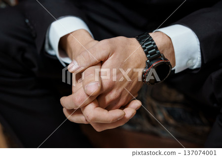 Close-up of a businessman's hands clasped together, wearing a black suit and smartwatch, showcasing professionalism and focus Close-up of a businessman's hands clasped together, wearing a black suit and smartwatch, showcasing professionalism and focus 137074001