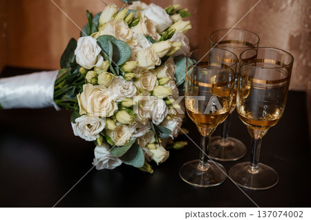 Elegant White Rose Wedding Bouquet with Champagne Glasses on Dark Table in Soft Lighting Elegant White Rose Wedding Bouquet with Champagne Glasses on Dark Table in Soft Lighting 137074002