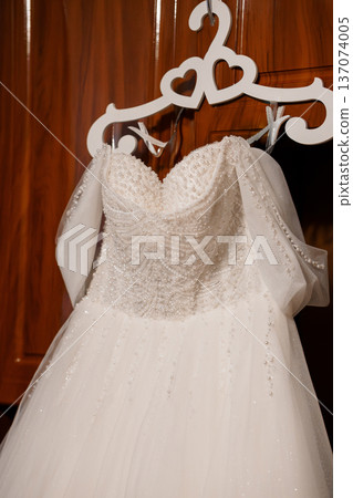 Elegant White Wedding Dress with Pearl Embellishments Hanging on Heart-Shaped Hanger Against Wooden Background Elegant White Wedding Dress with Pearl Embellishments Hanging on Heart-Shaped Hanger Against Wooden Background 137074005