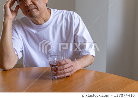 Senior man holding a glass and holding his head Senior man holding a glass and holding his head 137074416