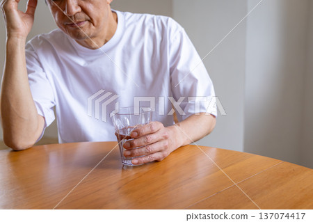 Senior man holding a glass and holding his head Senior man holding a glass and holding his head 137074417
