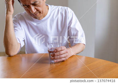 Senior man holding a glass and holding his head 137074418