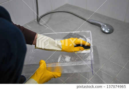 Cleaning refrigerator glass shelf with sponge and rubber gloves in bathroom sink Cleaning refrigerator glass shelf with sponge and rubber gloves in bathroom sink 137074965