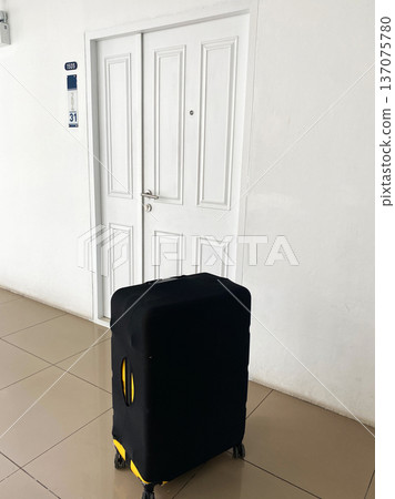 Black suitcase with yellow accents positioned in front of a closed white door in a hallway of a rented apartment, number 31 visible on the wall Black suitcase with yellow accents positioned in front of a closed white door in a hallway of a rented apartment, number 31 visible on the wall 137075780