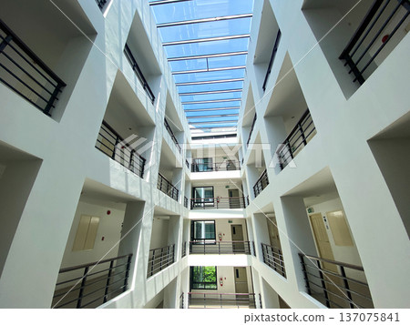 Modern architectural design of an indoor atrium featuring multiple floors, balconies, and a glass roof allowing natural light to illuminate the space 137075841
