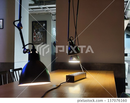 Modern interior features a wooden table with hanging pendant lamps casting direct light. The space includes black chairs with vertical slats 137076160