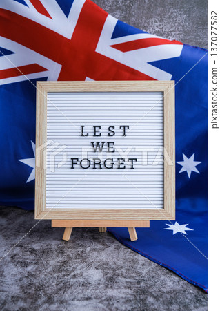 Somber Australian flag backdrop with text LEST WE FORGET on letter board. Respectful message for memorial ANZAC. Concept of remembrance and honor Somber Australian flag backdrop with text LEST WE FORGET on letter board. Respectful message for memorial ANZAC. Concept of remembrance and honor 137077582