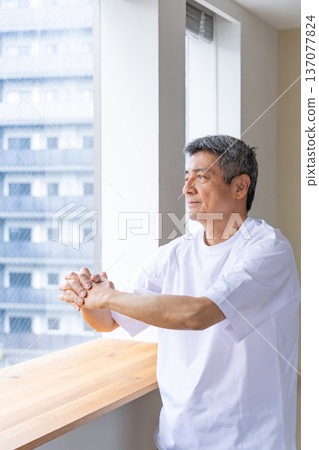 一位老人在窗邊伸展身體。 一位老人在窗邊伸展身體。 137077824