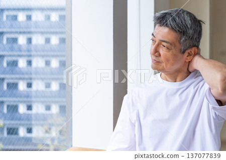 一名老年男子在窗邊摀著脖子。 137077839