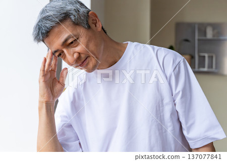 一位老人在窗邊摀著頭。 137077841