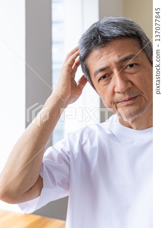 Senior man holding his head by the window 137077845