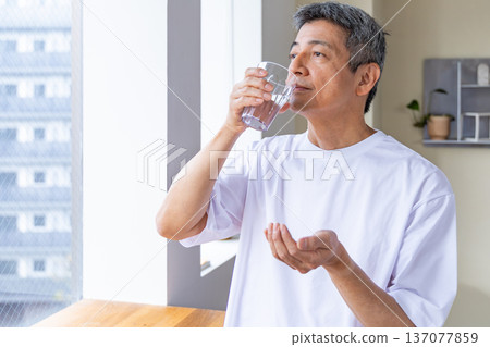 Senior man taking medicine by the window Senior man taking medicine by the window 137077859