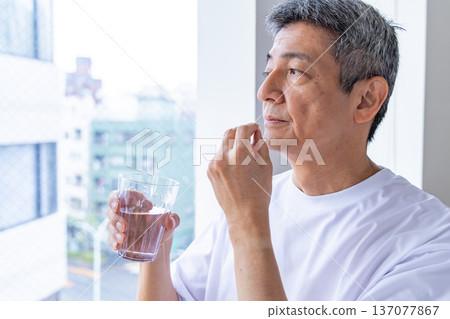 Senior man taking medicine by the window Senior man taking medicine by the window 137077867