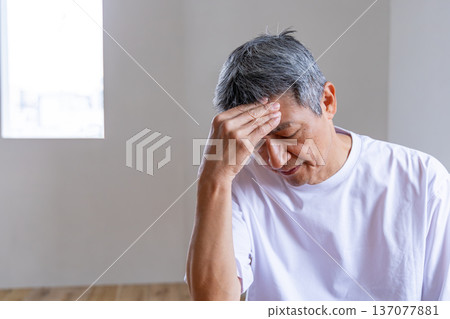 Senior man holding his head in the living room Senior man holding his head in the living room 137077881