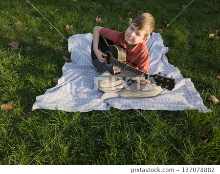 Guitar lesson for children in park, boy playing acoustic guitar outdoors during kids leisure and childhood education activity Guitar lesson for children in park, boy playing acoustic guitar outdoors during kids leisure and childhood education activity 137078882