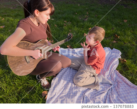 Guitar lesson for children outdoors in park, childhood education and kids leisure activity concept Guitar lesson for children outdoors in park, childhood education and kids leisure activity concept 137078883