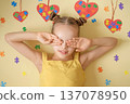 A shy, modest girl with autism covers her face with her hands. The background is decorated with hearts and pieces of colorful colorful puzzles - an autistic symbol 137078950