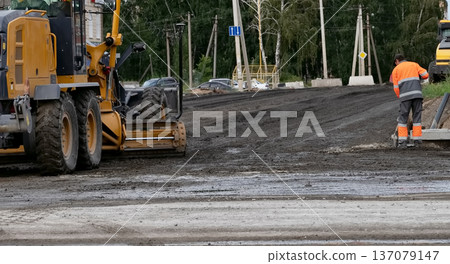 Construction machinery operates on a road at a work site in an urban area during daylight hours 137079147